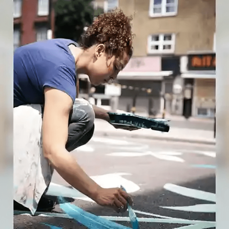 A woman painting on the street with blue paint.